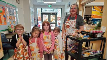 Four young children wearing aprons stand beside a woman wearing an apron.