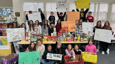 Students holding up signs and posing with their food bank donation haul.
