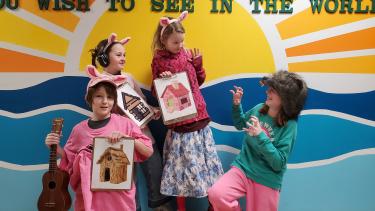 three students dressed as the three little pigs and one student dressed as a wolf posing for a picture, the pigs look scared of the wolf