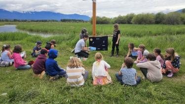 Students outside at wildlife centre, sitting in a circle looking at a demonstration of info from leader