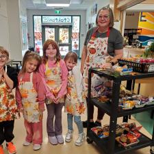 Four young children wearing aprons stand beside a woman wearing an apron.